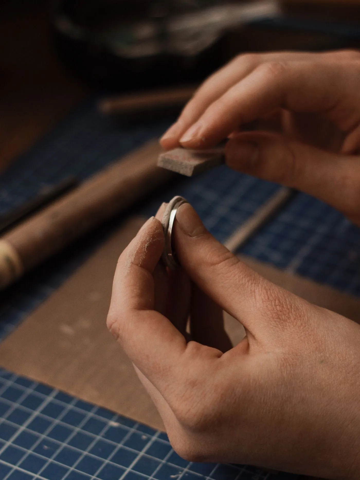 A bare silver band being filed flat with an emery stick at the bench.