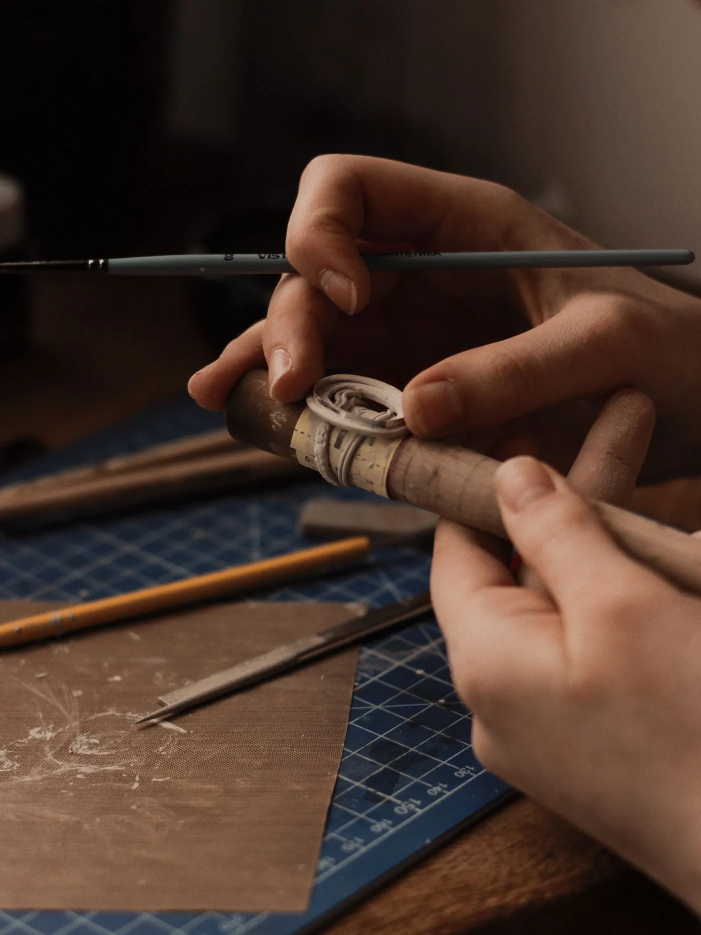 The silver band wrapped in paper tape on a wooden ring mandrel, being marked up at the bench.