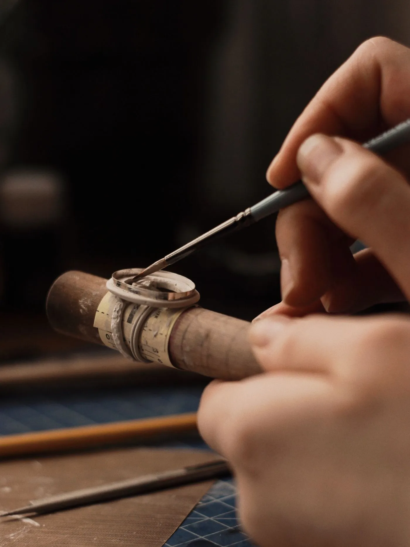 A fine brush applying flux to the silver band on the mandrel with the stone setting sitting on top.