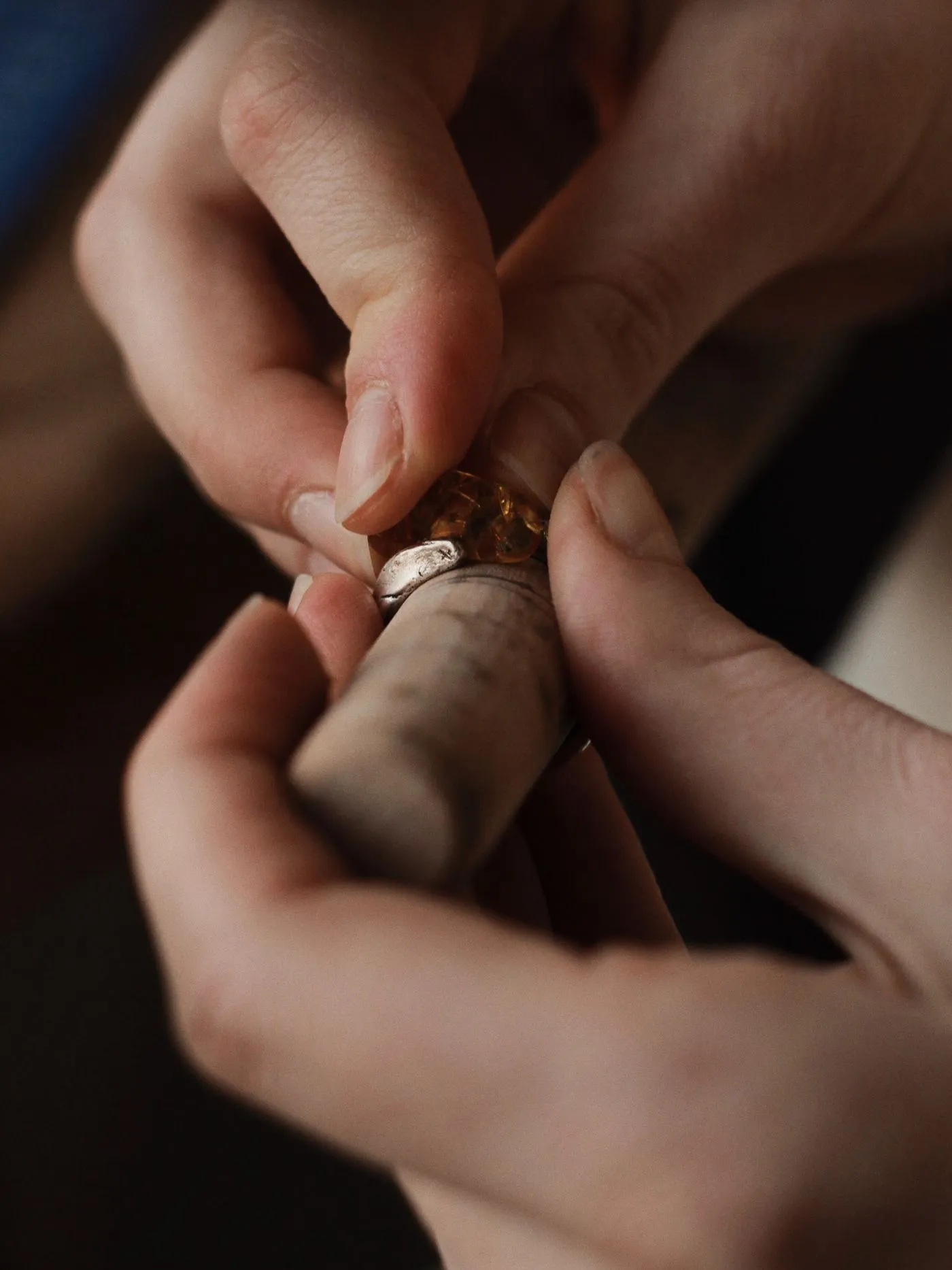 Two hands setting a stone into a silver bezel on the bench.