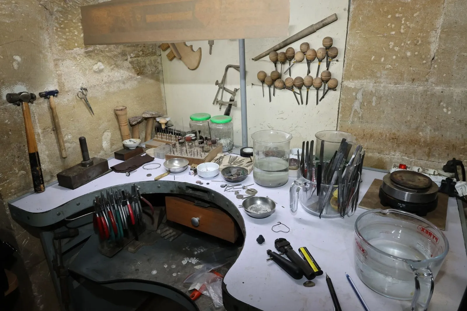 A jeweller's bench seen head on, with pliers and files racked along the wall above it.