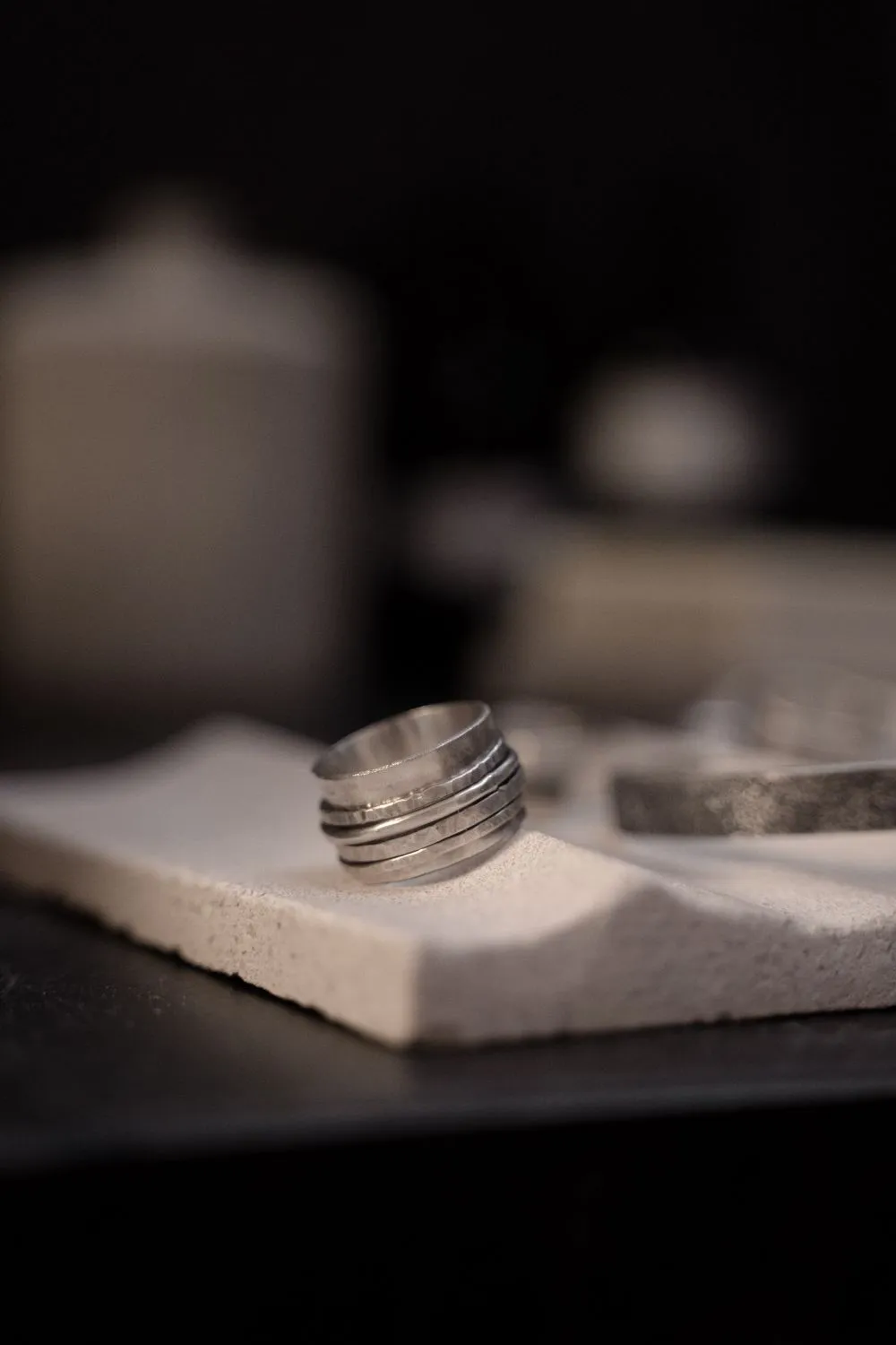 A wide hammered sterling silver band standing on a plaster tile.
