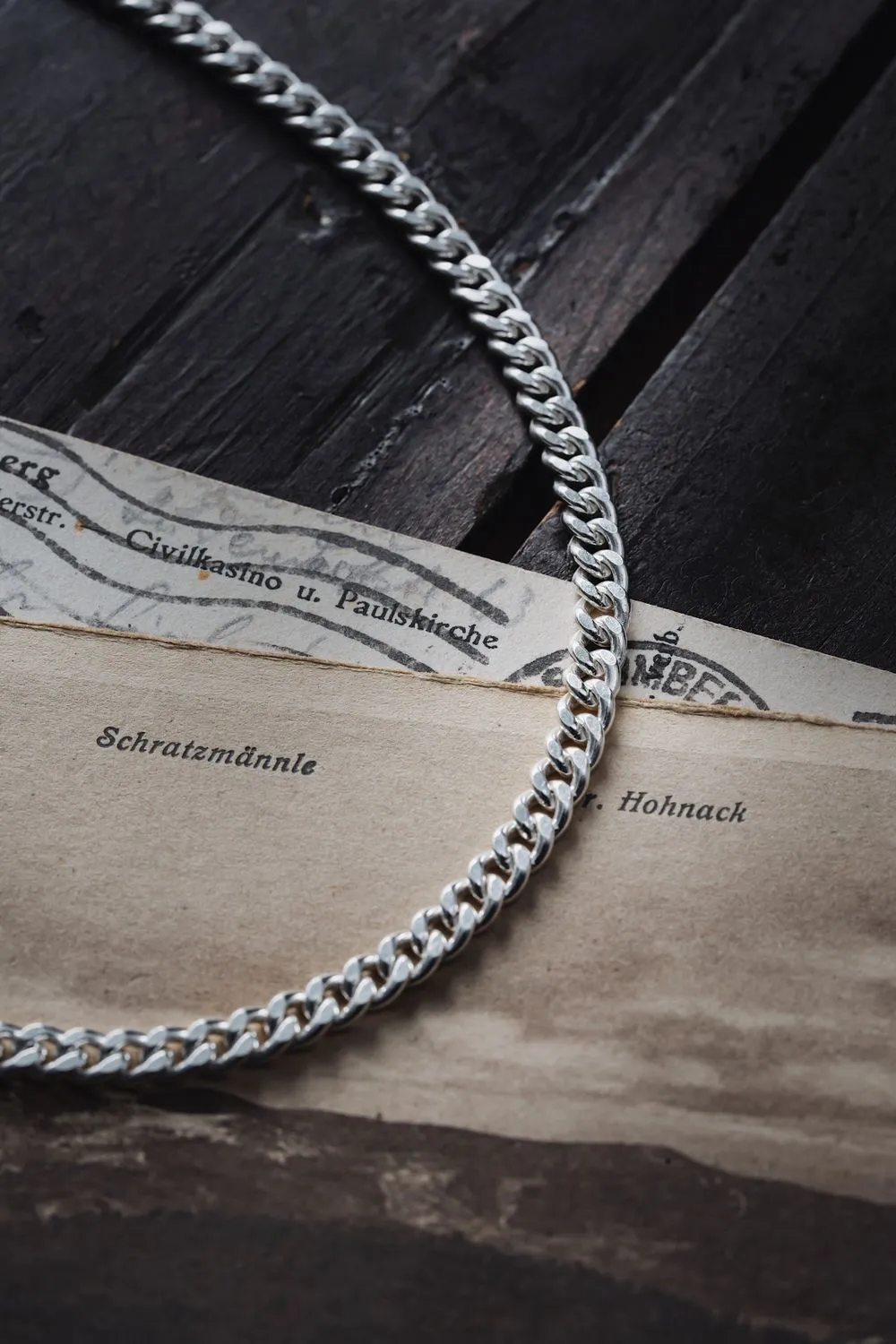 A heavy silver curb chain lying across an old printed map.
