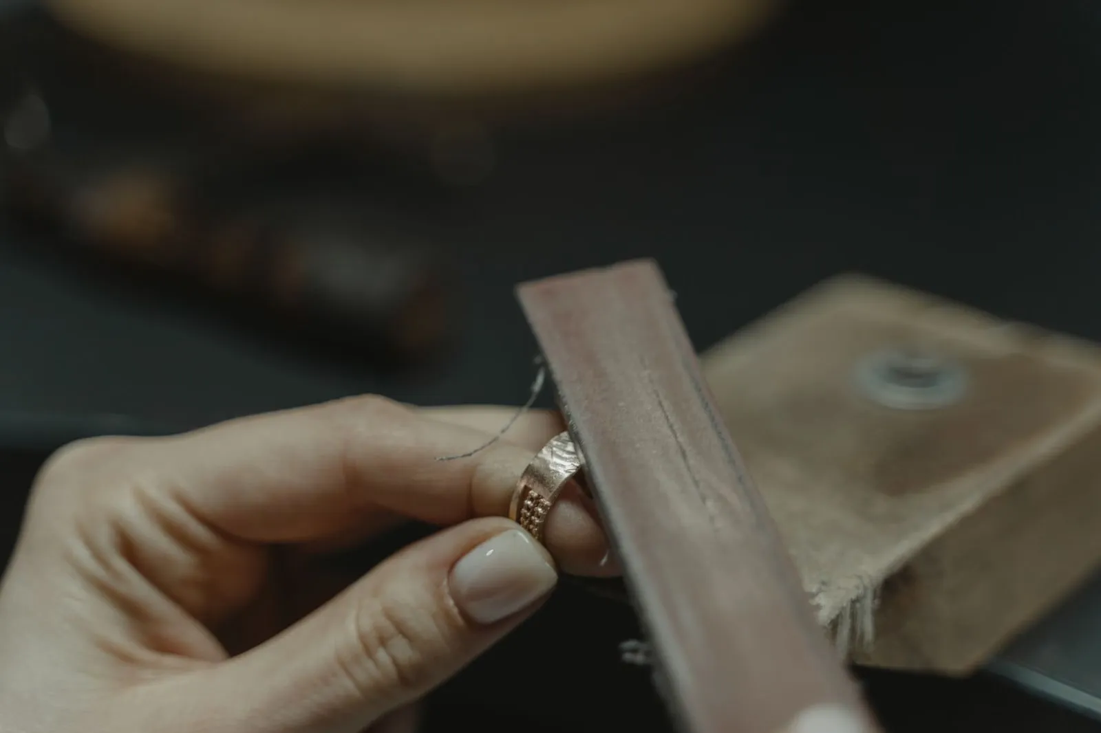 Two hands working an emery stick along the edge of a silver band.