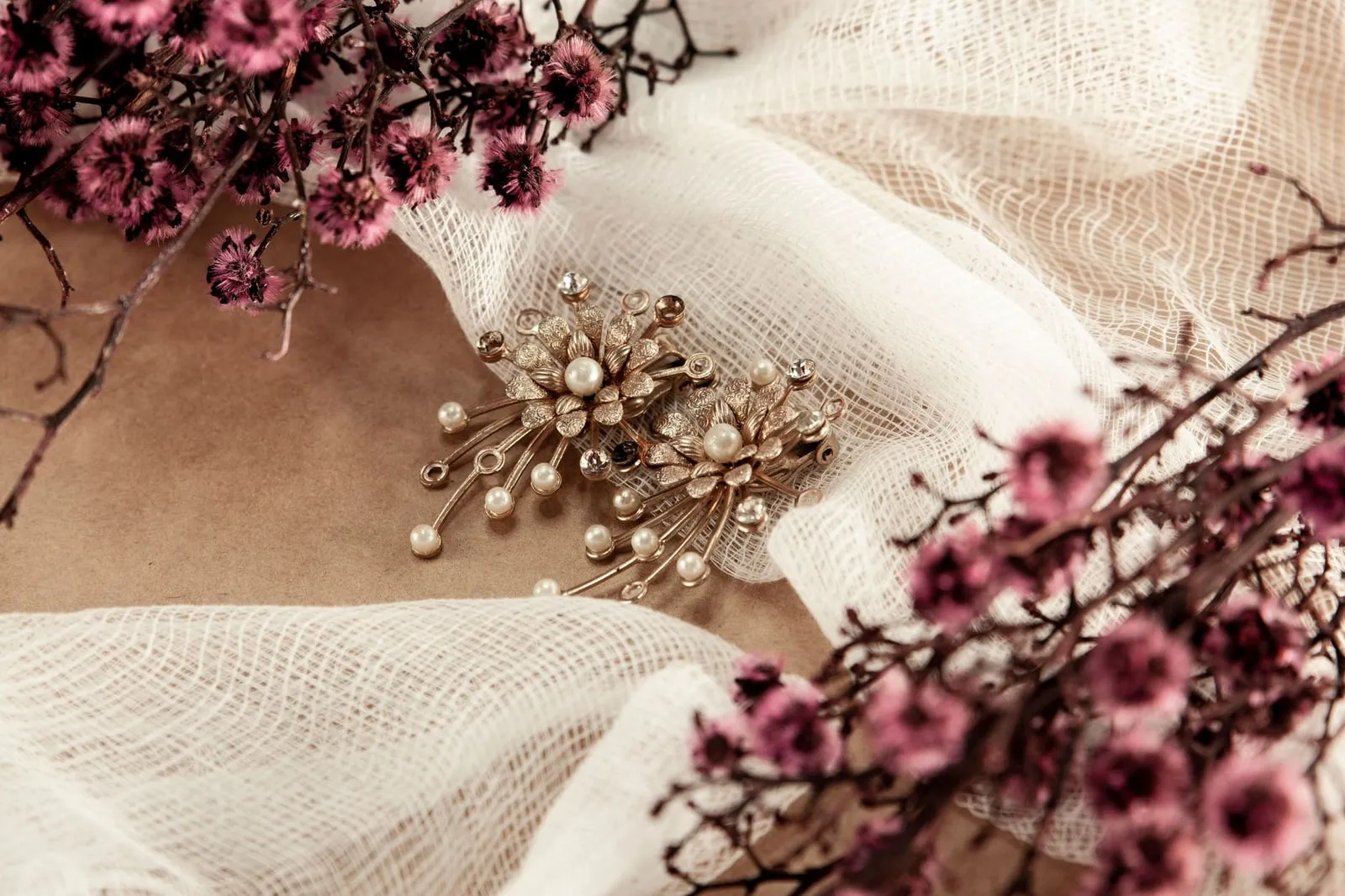 An antique pearl and diamanté brooch lying on cream cloth beside dried flowers.