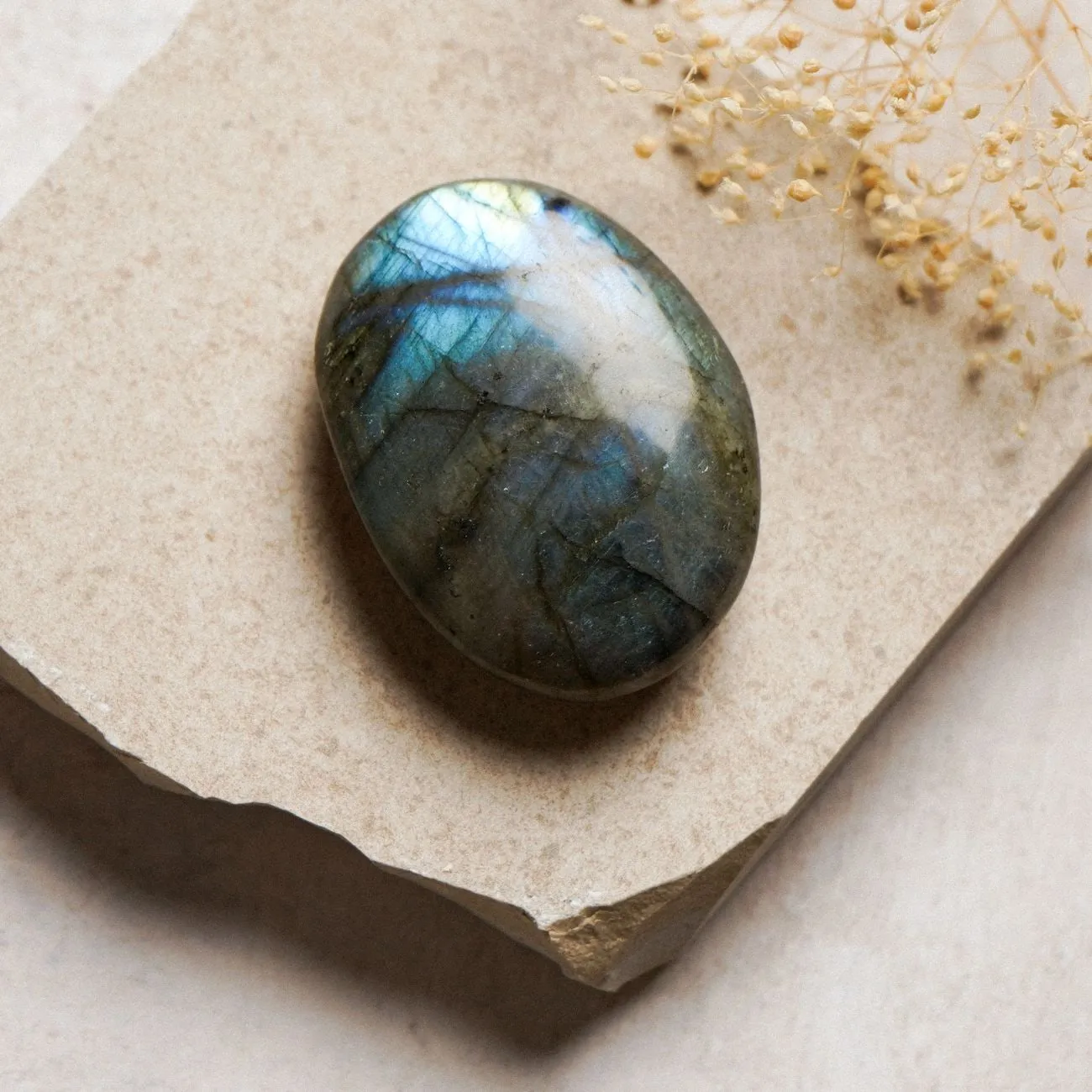 A polished labradorite cabochon on a pale stone slab, its blue flash catching the light.