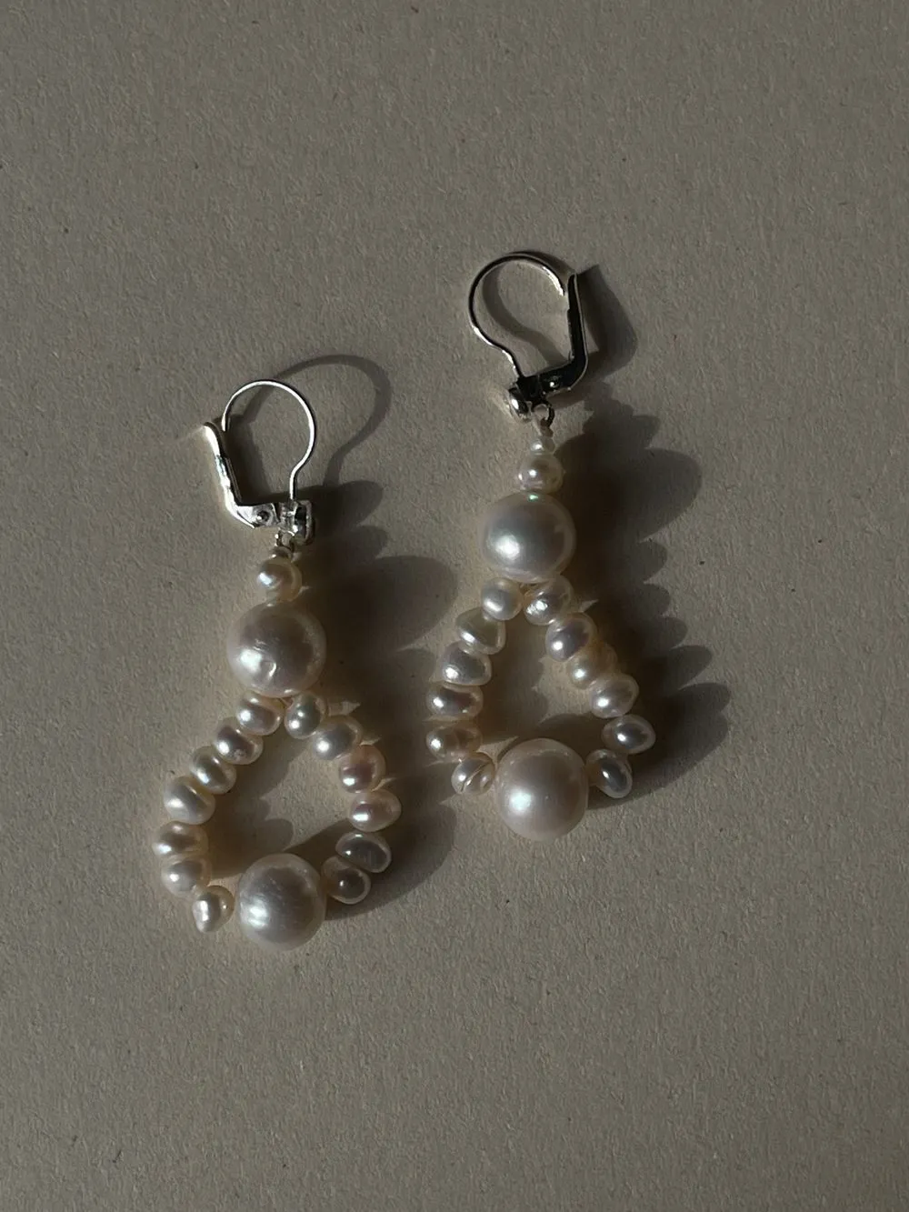 A pair of freshwater baroque pearl drop earrings on silver hooks, on oat-coloured paper.