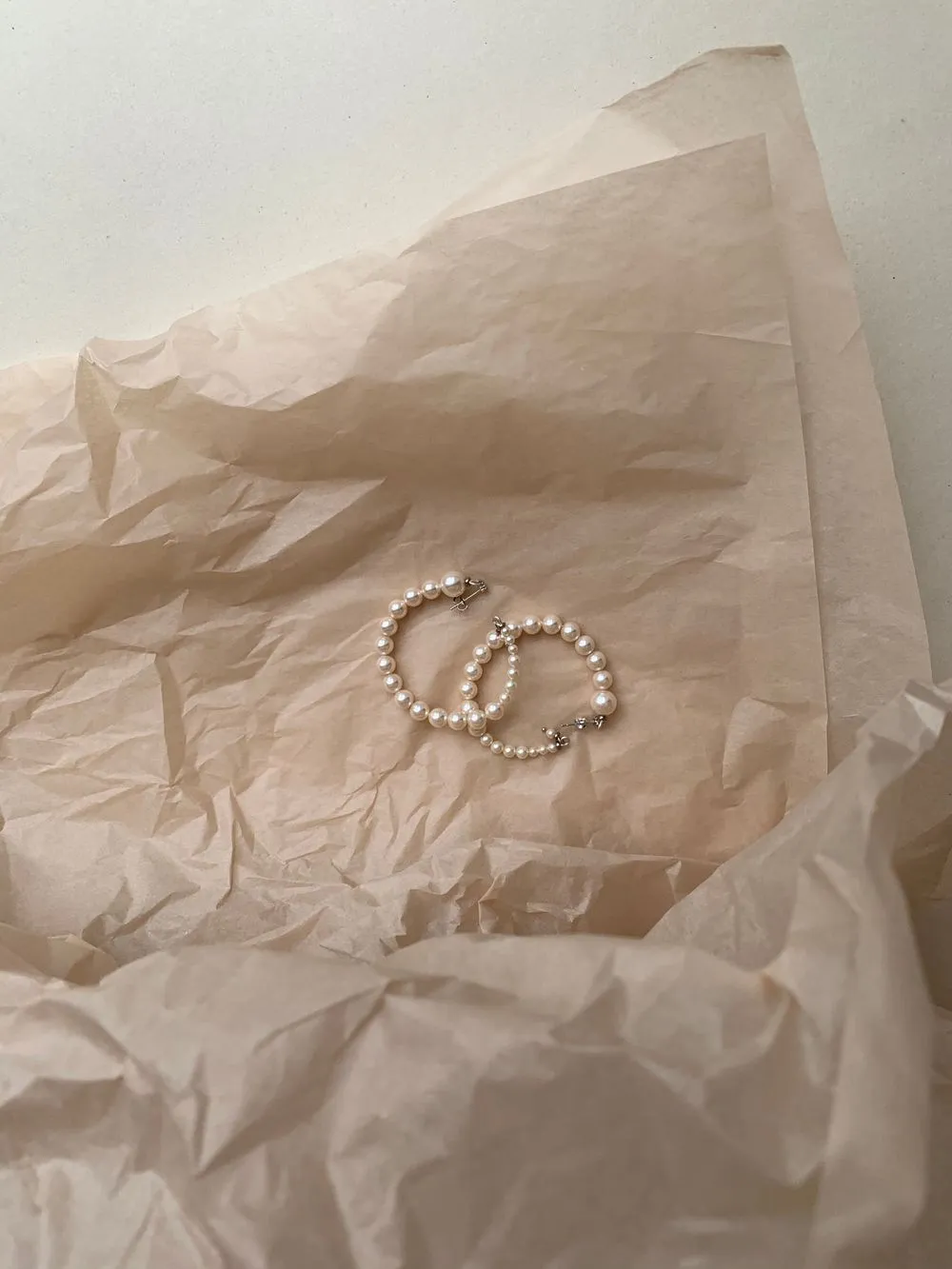 Two small hoops closely strung with pale freshwater seed pearls, resting on crumpled tissue paper.