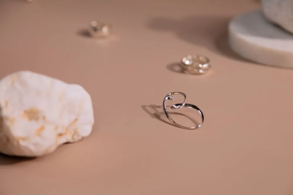 A fine silver band photographed on a warm sand-coloured ground beside a pale stone.