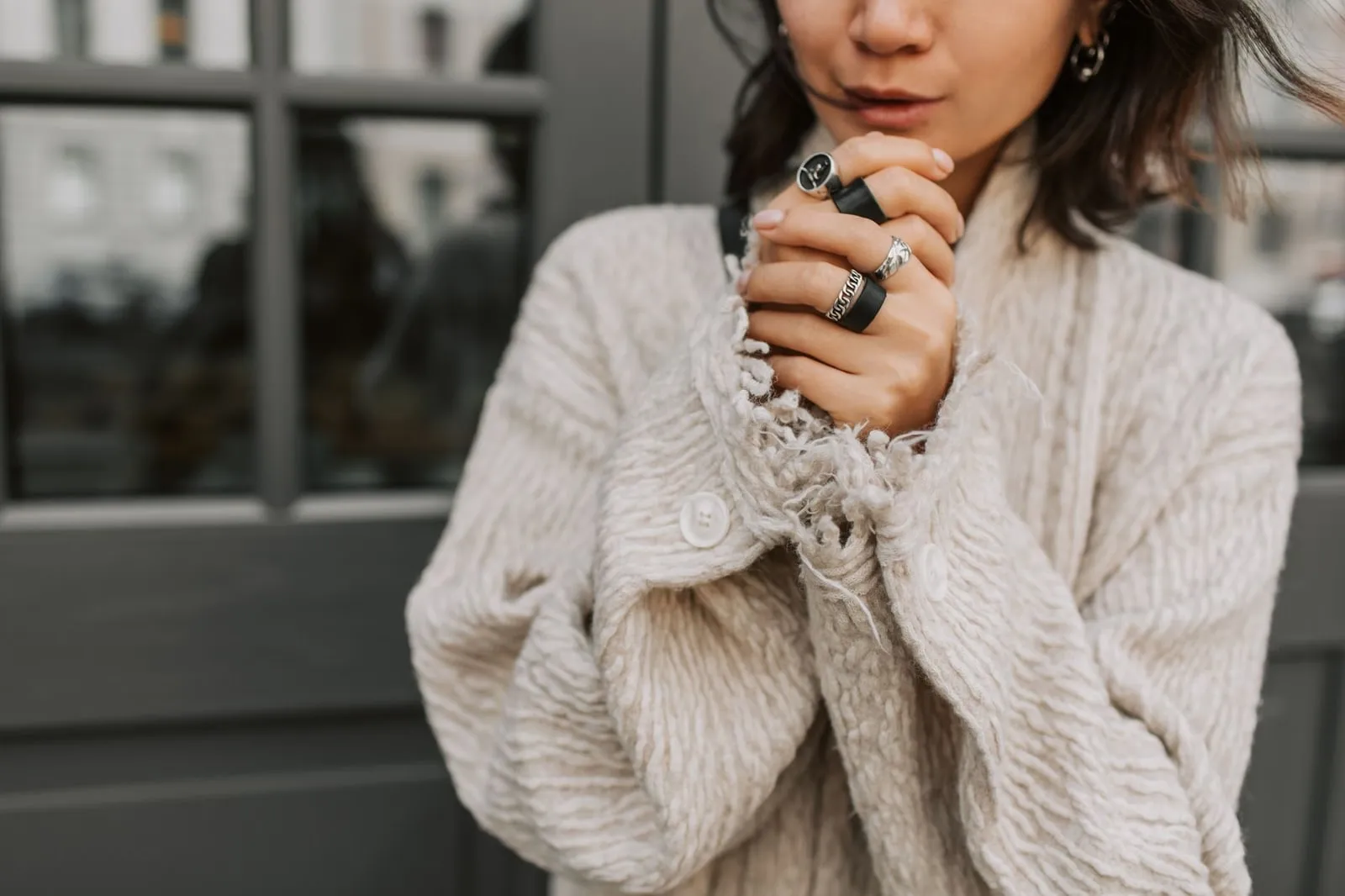 A person in an oatmeal knit jumper, hands together, wearing several slim silver rings.